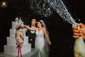 Um casal corta o bolo de casamento no Palácio do Bósforo, em Istambul, com champanhe borrifando em primeiro plano, um momento de celebração e alegria.